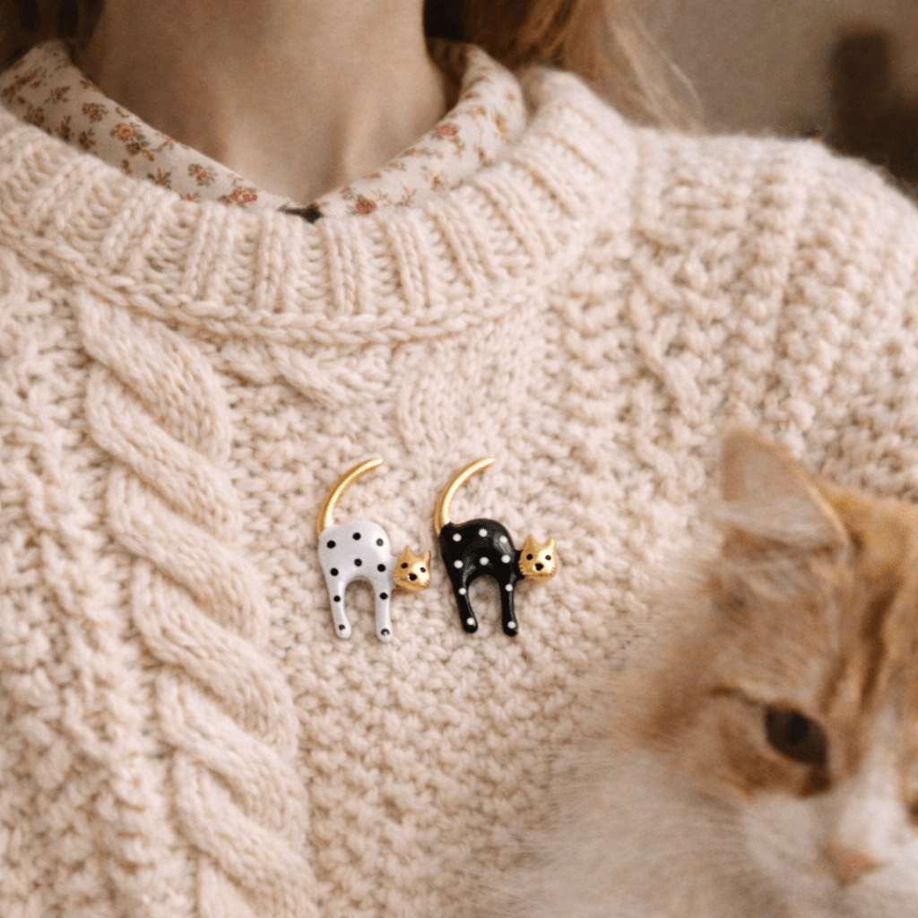 Person wearing vintage styled black and white cat brooches on a beige sweater.
