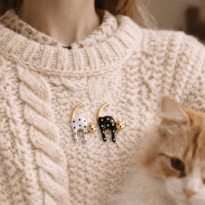 Person wearing vintage styled black and white cat brooches on a beige sweater.