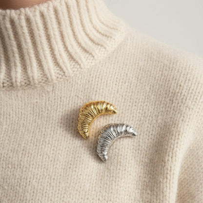 Gold and silver croissant brooches on a cream high neck chunky jumper 