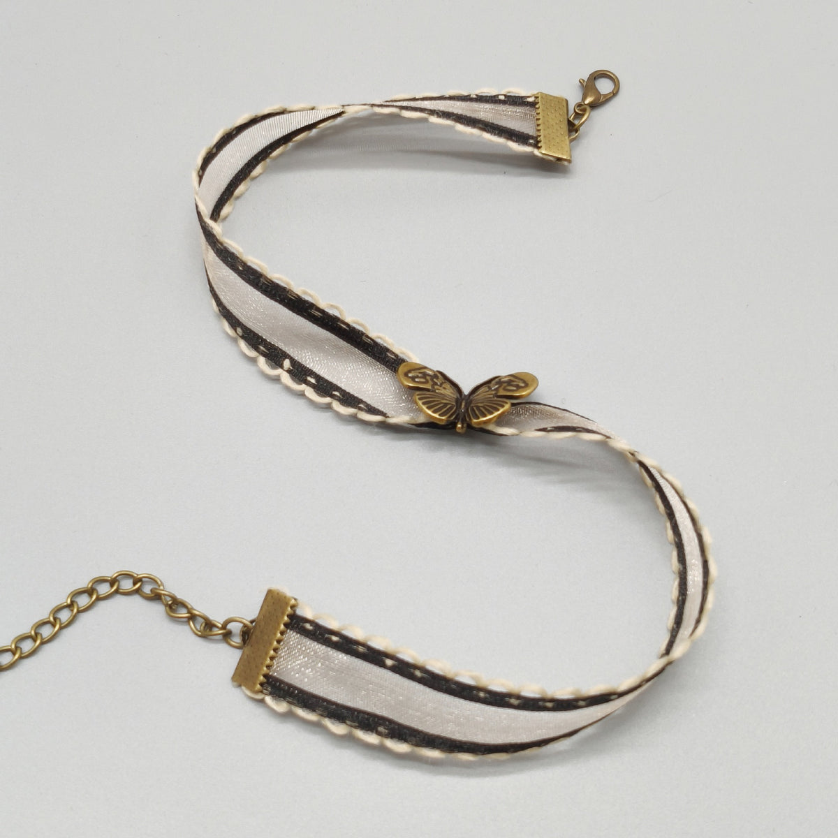 flat lay of an Ivory organza ribbon choker with antique bronze butterfly charm