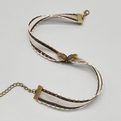 flat lay of an Ivory organza ribbon choker with antique bronze butterfly charm