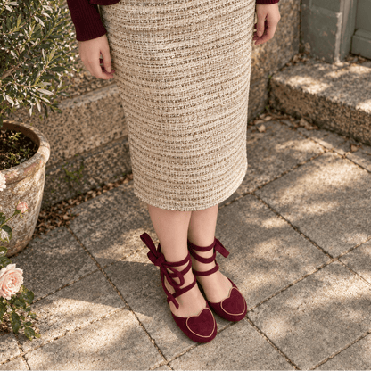 A person wearing a beige and brown textured knit pencil skirt with a dark burgundy top and matching burgundy heart-shaped lace-up shoes, standing on stone pavers next to a potted plant.