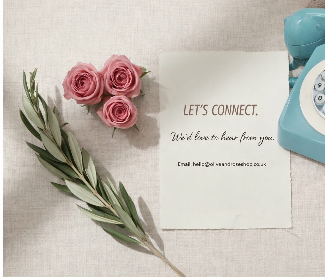 A table layout for contact us page, roses, olives leaves, a note, a pen, and a vintage phone on the table.