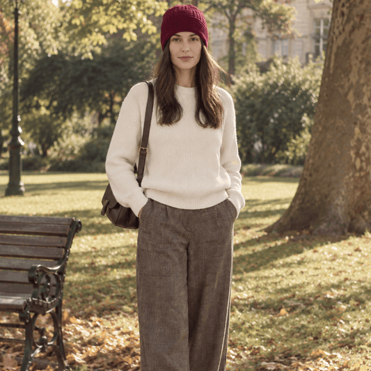 A woman wearing a burgundy merino beanie with a cream knit sweater and tweed trousers in the park