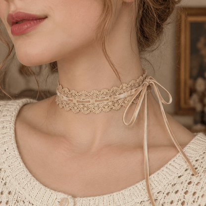 A close-up of a woman wearing a delicate beige lace choker with thin ribbon ties, paired with a cream-colored knit cardigan.