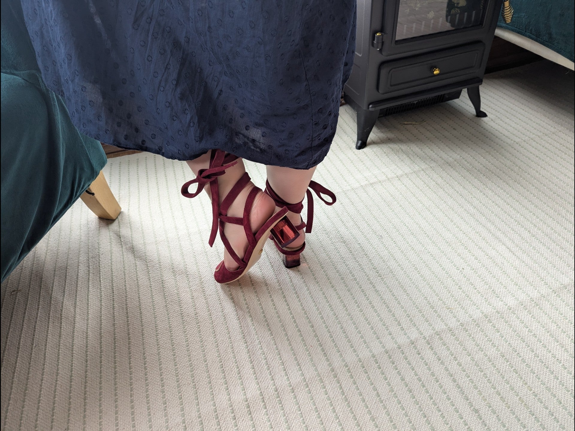 Model wearing mid-heeled burgundy suede ankle tie pumps on a carpeted floor