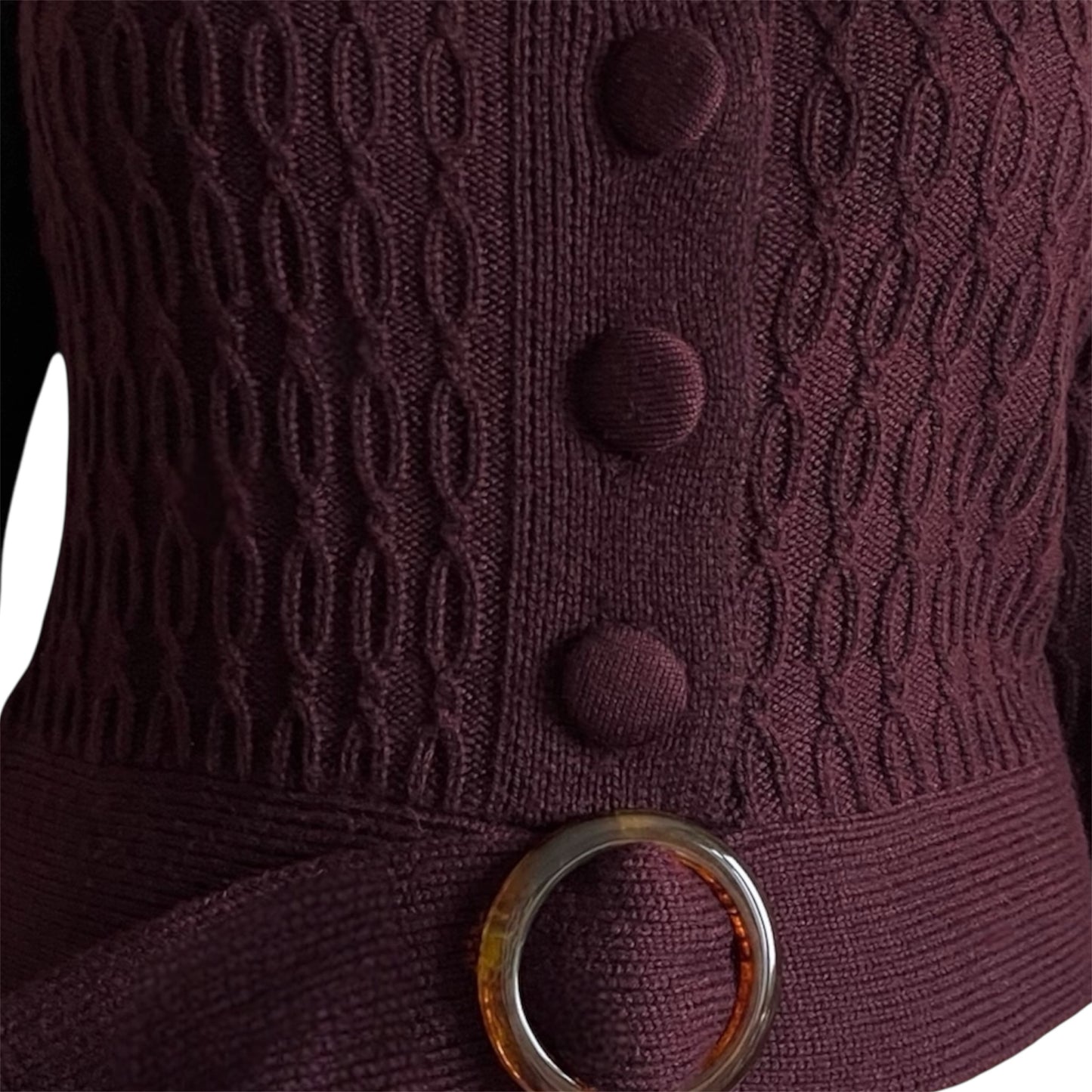 Close-up of a dark purple chunky cardigan with knit covered buttons and a matching belt.