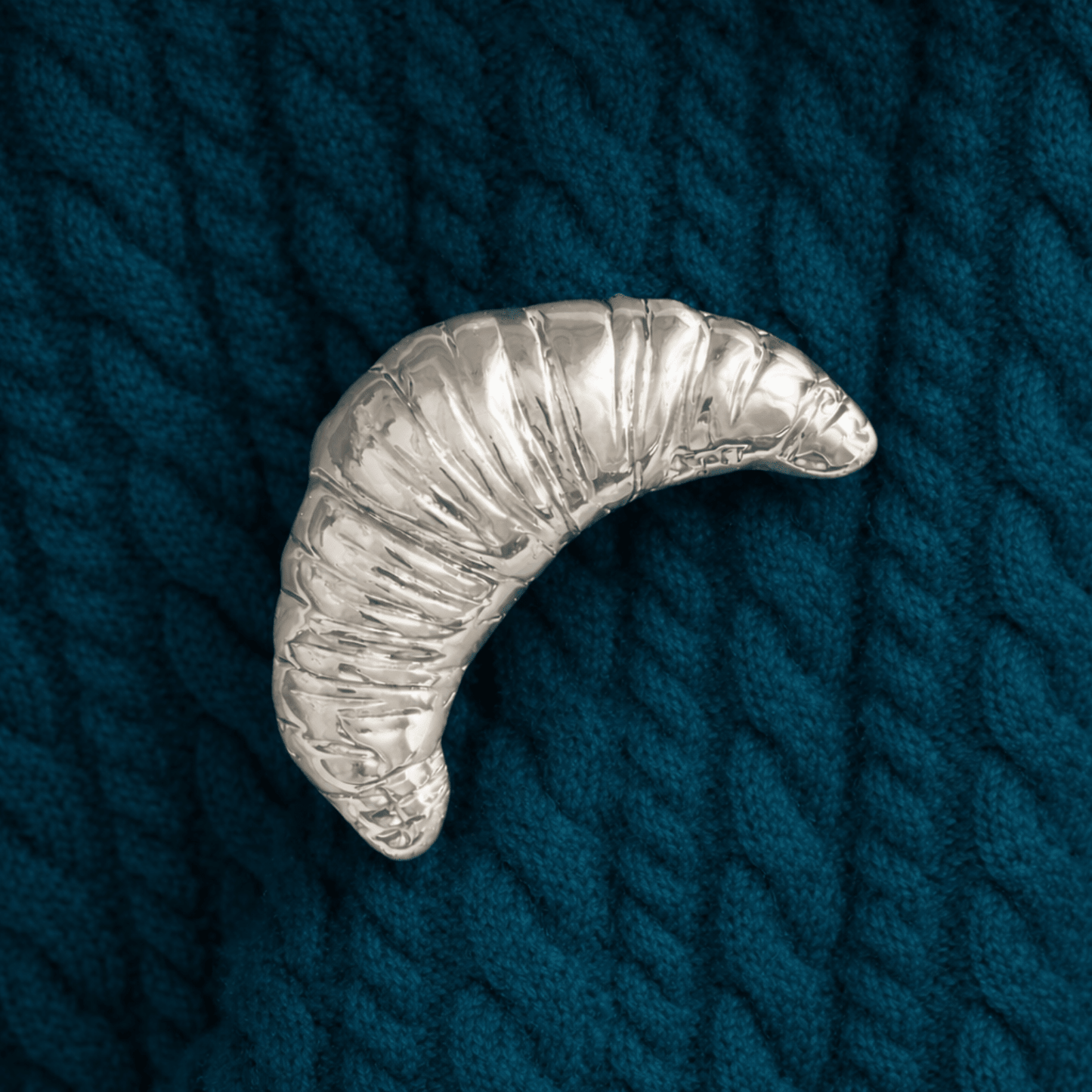 Silver crescent-shaped brooch on a textured blue fabric background