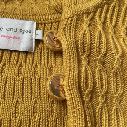 Close-up of a mustard yellow knitted cardigan with a brand label and knit covered button details